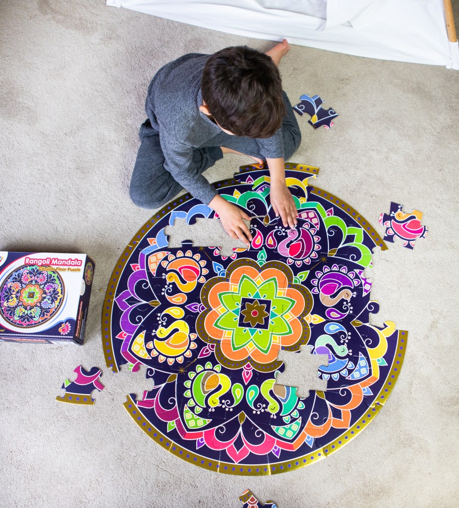 Boy building a giant circular rangoli mandala floor puzzle on the carpet, a mess-free rangoli for Diwali